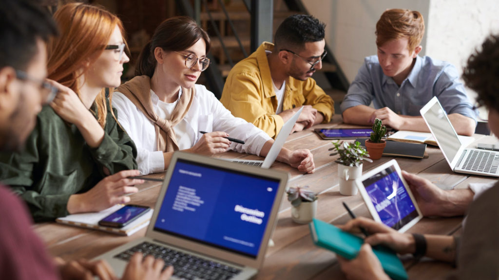 a group of people sitting around a table with laptops