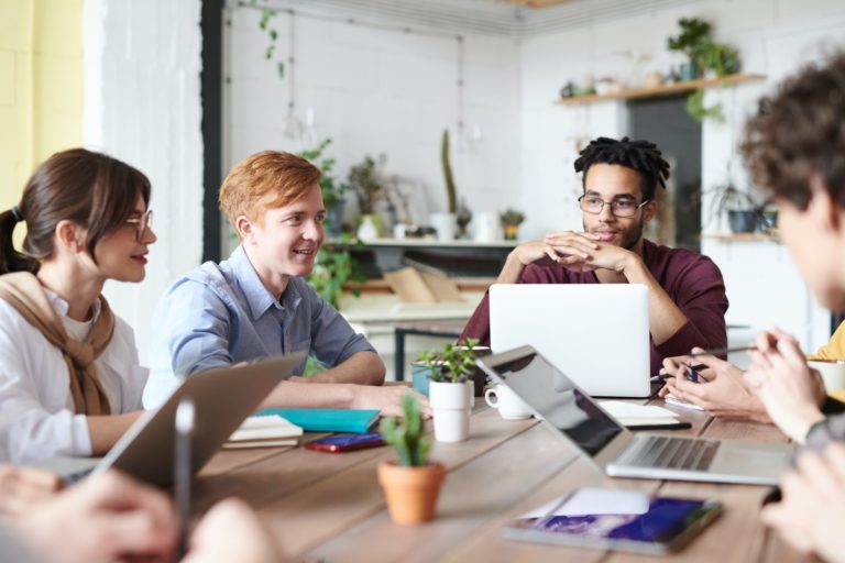 a group of people sitting around a table with laptops