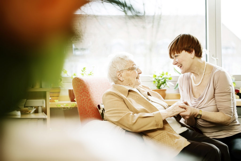 Adult daughter talking to her mother with Alzheimer's disease in her room at retirement home