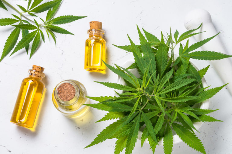 Cannabis oil in glass bottles and cannabis leaves at white table